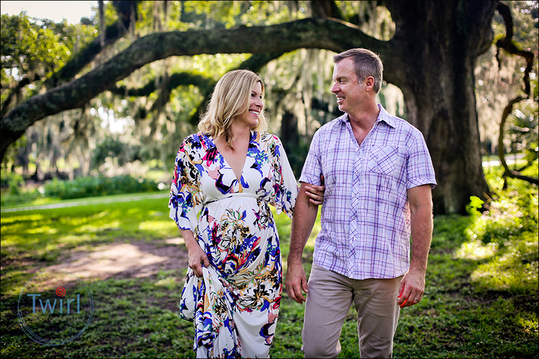 Husband and wife with pregnant belly walking in front of a large Oak tree in New Orleans. 