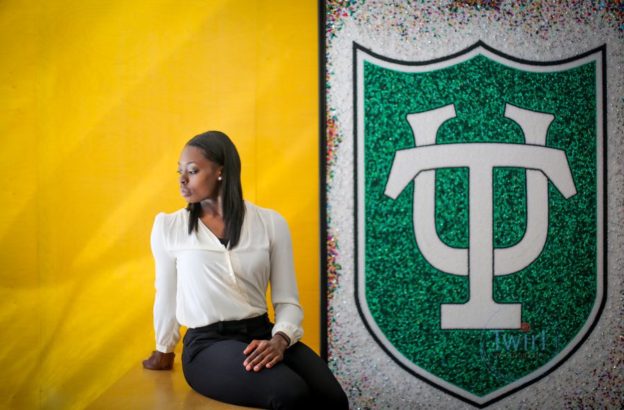 A graduate student at Tulane University sitting next to a Tulane sign and a yellow wall for a professional portrait.