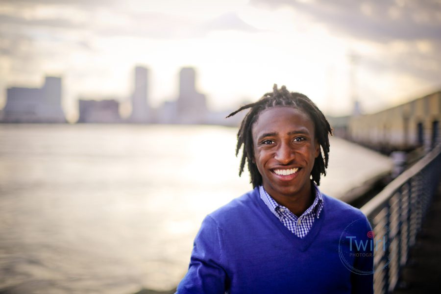 A man posing for a professional portrait in New Orleans with the skyline behind him along the Mississippi river.