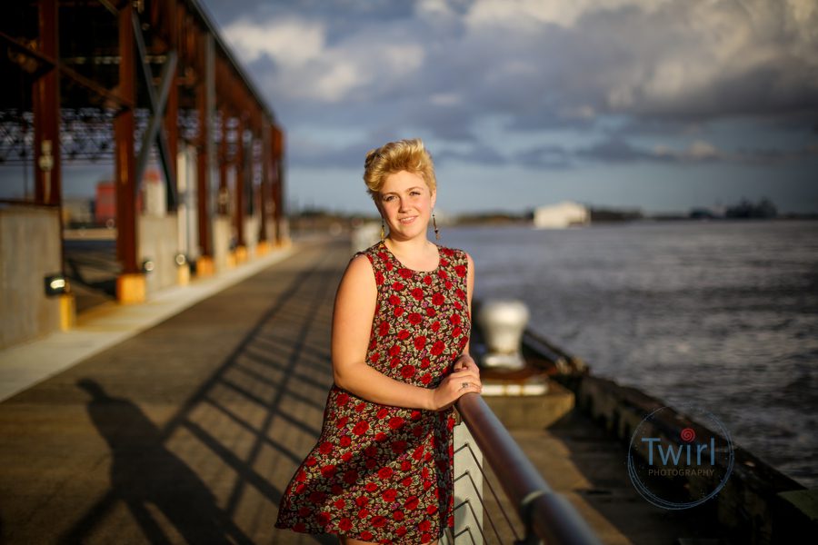 A young professional with a red dress in the sunset leaning against the railing at the Mississippi River for a photo.