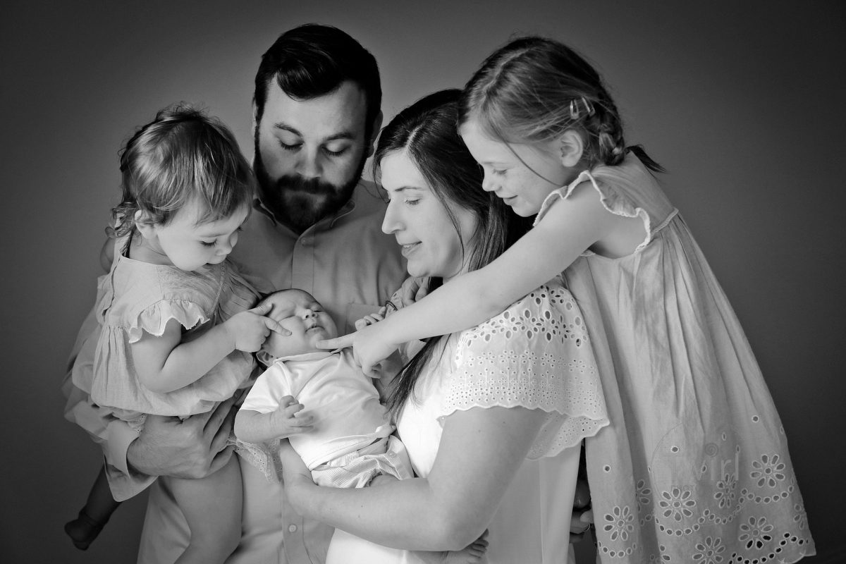 Family of five looking at their newborn baby brother with mom and dad and two sisters in their New Orleans home.