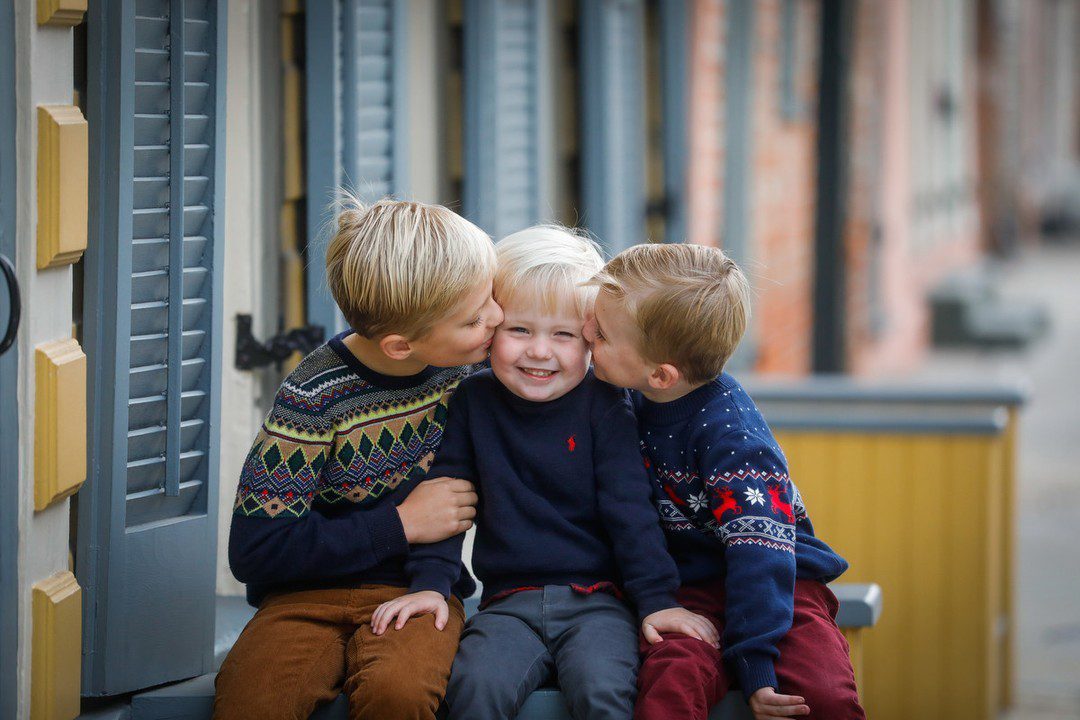 Three brothers, the older two kissing the youngest, around 3 years old wearing navy blue sweaters.