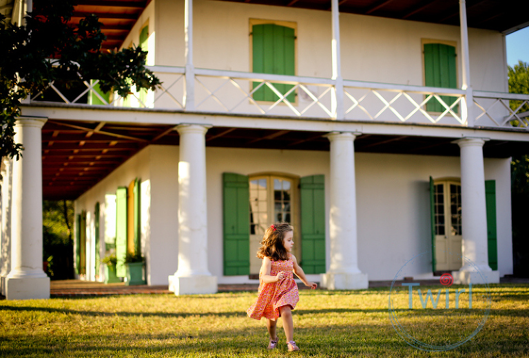 A girl running in a Spring dress with a red bow at sunset in front of the Pitot House for Family Portraits in New Orleans.