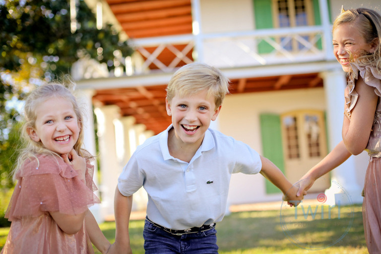 Three siblings laughing as they run in front of the white and green shutter historic home in Bayou St. John for photos.