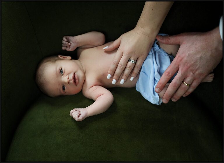 Newborn baby with mom and dad's hands on it's belly during newborn photos.