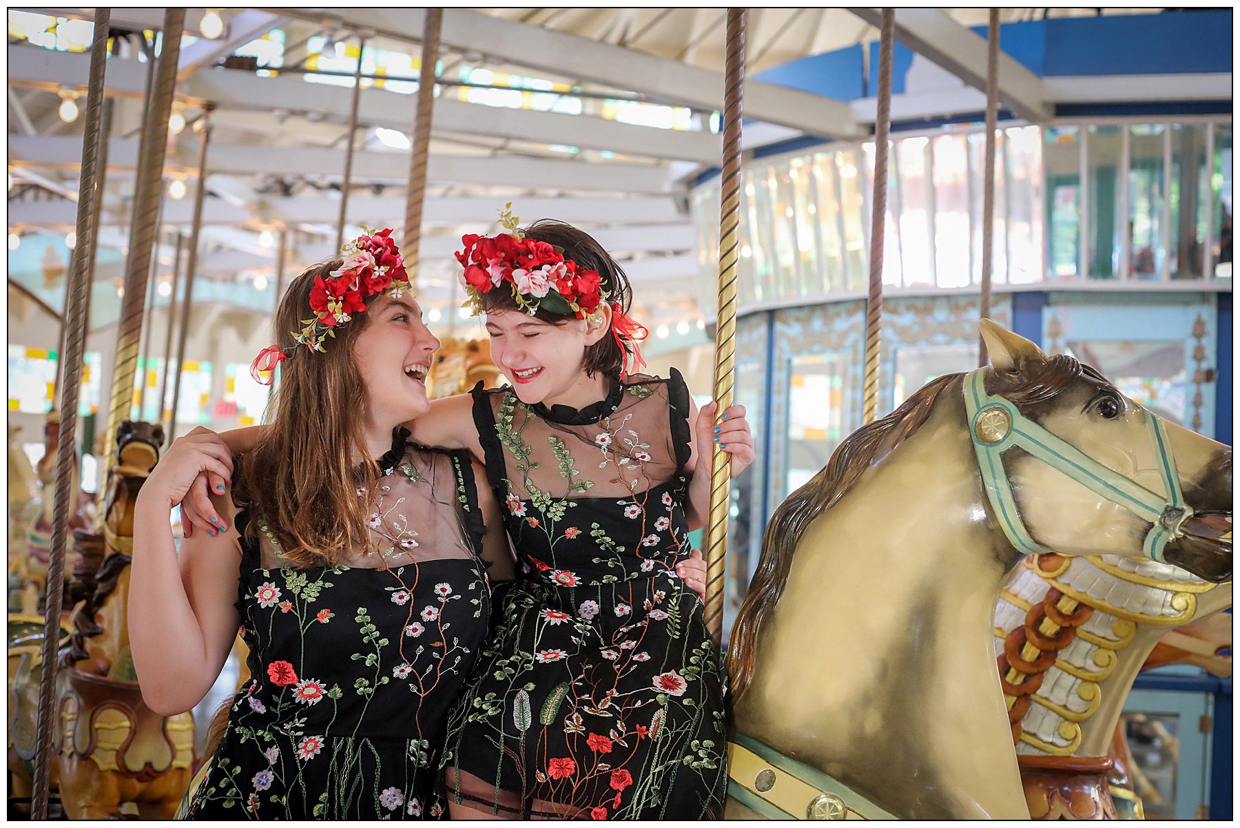 Two sisters laughing with each other in a carousel wearing black and red dresses.
