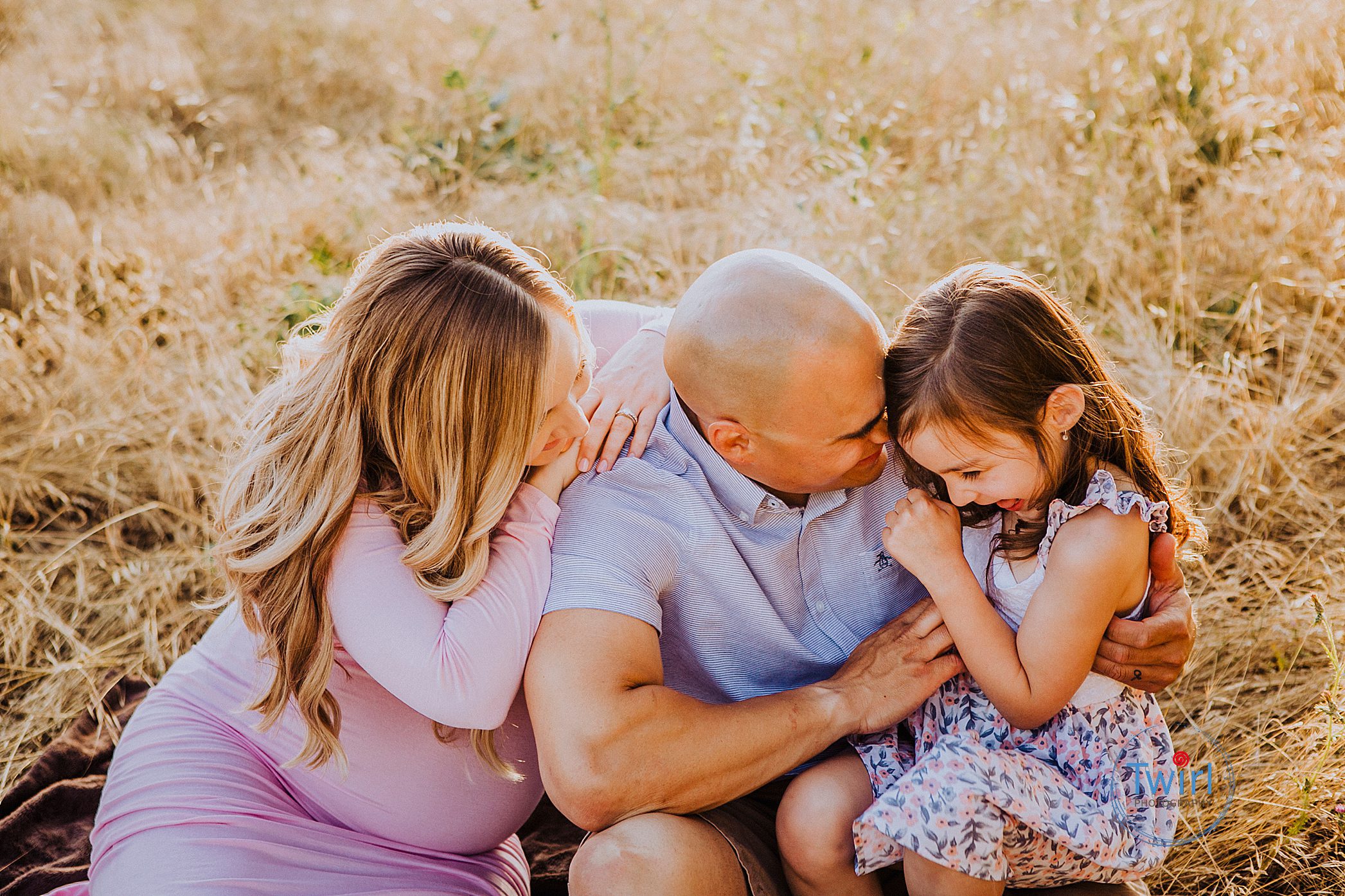 A pregnant mom and dad laughing and hugging their young daughter in a field for photos on 5-tips for maternity portraits in New Orleans.