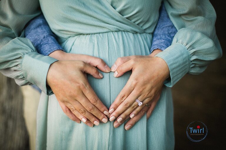 A detail photos of a mom and dad with their hands on mom's pregnant belly while wearing a textured crepe dress for maternity photos in New Orleans.