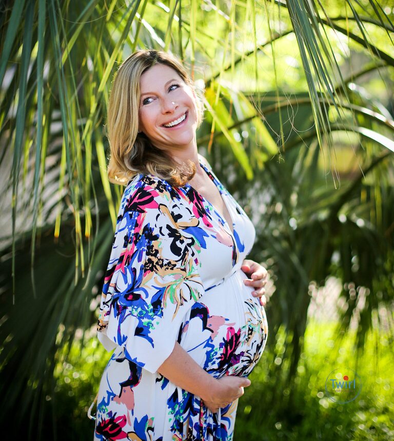 A pregnant woman holding her belly while wearing a printed floral maxi dress for maternity photos in City Park in New Orleans.