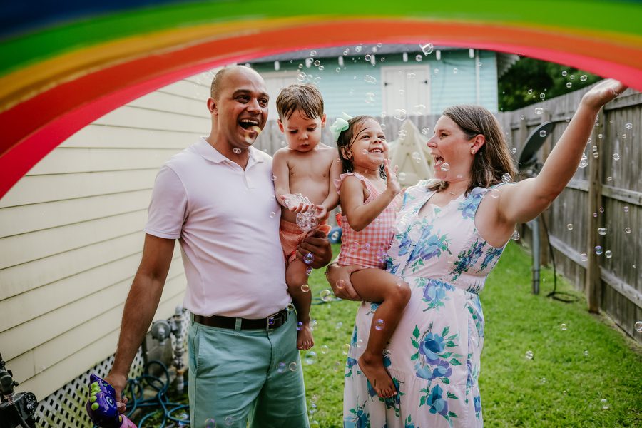 A mom and dad holding their your son and daughter under a sprinkler rainbow for fun family summer photos in New Orleans.