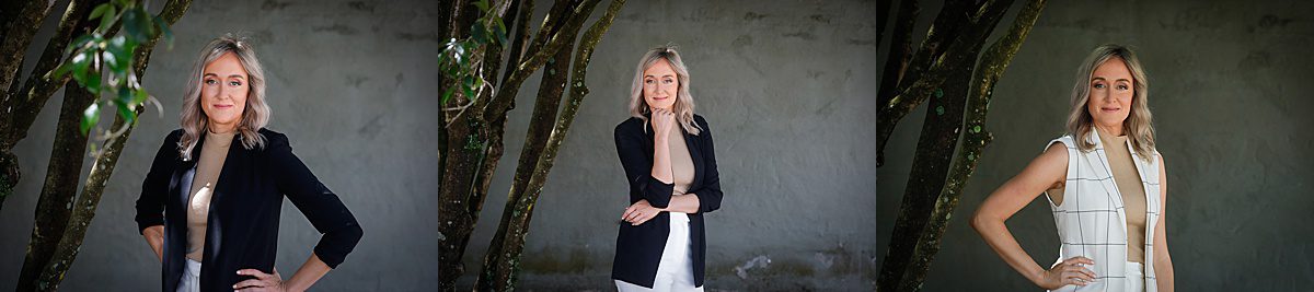 A woman posing for a business portrait in New Orleans wearing a black blazer in front of a grey wall.