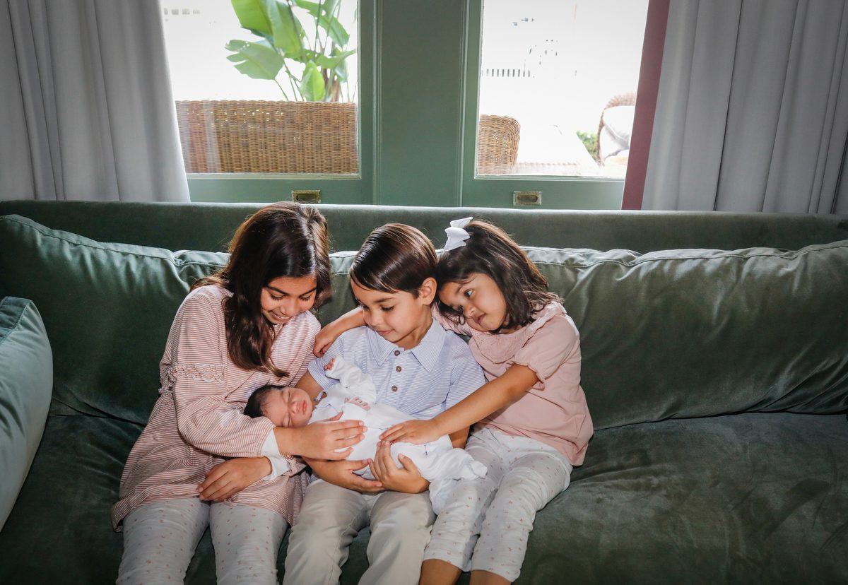 Three older siblings holding their new baby sister during newborn pictures in their New Orleans home for photography studio Twirl Photography.