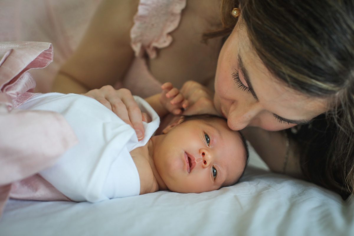 A mom reaching over to kiss the forehead of her new baby girl during newborn photos with Twirl Photography in New Orleans.