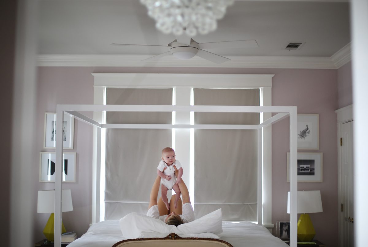 A mom lifting up her baby as she lays on the bed of her master bedroom with pastel decor for newborn photos by New Orleans photography studio Twirl Photography. Perfect Outfits for Your Lifestyle Newborn Photos in New Orleans.