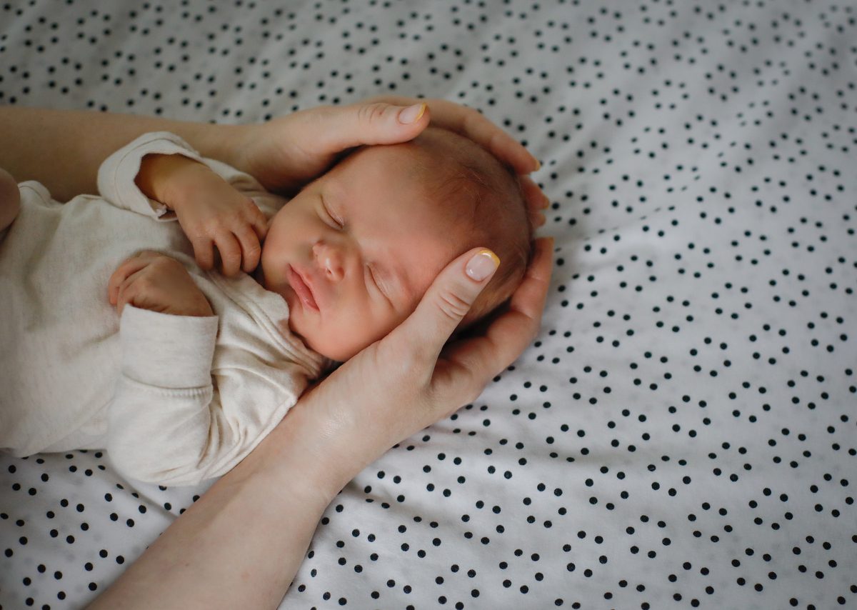 A close up of a newborn baby's face as with mom's hands during in home New Orleans lifestyle newborn session with Twirl Photography.