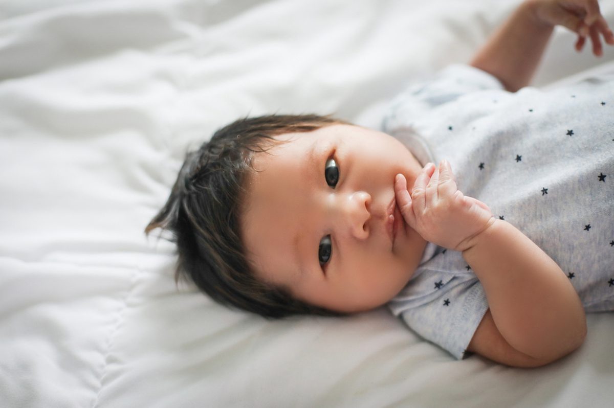 A newborn boy wearing a onesie and looking at the camera during his newborn photos by New Orleans photo studio Twirl Photography.