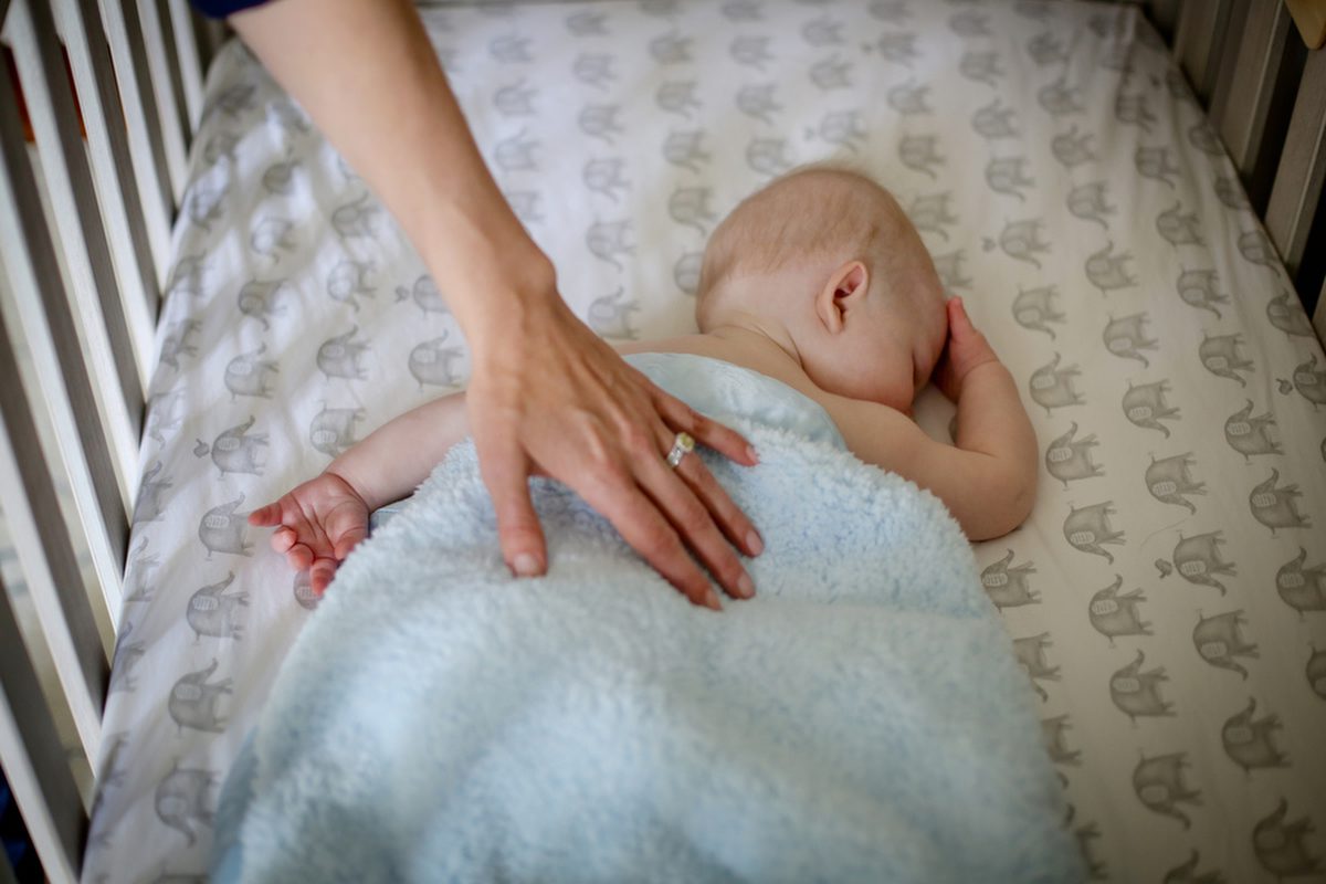 A mom's hand reaching down over a crib and caressing the back of her newborn boy.