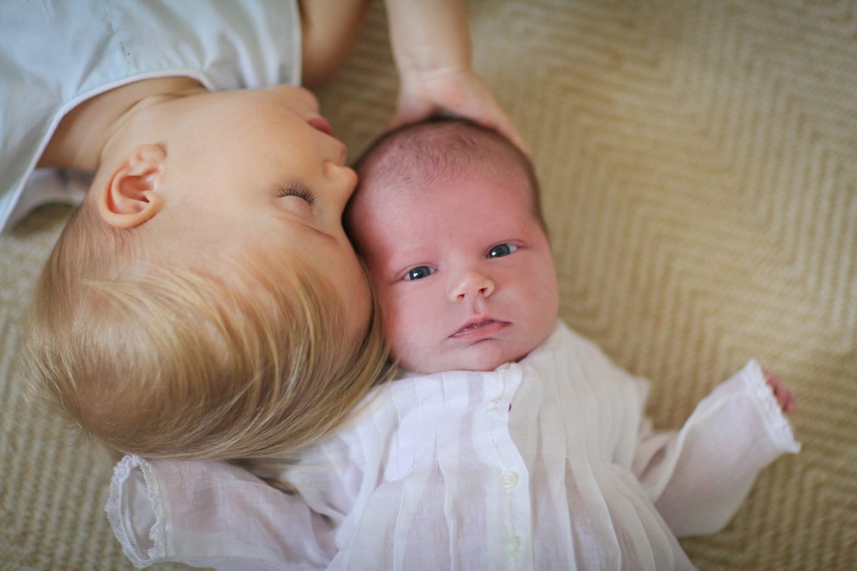 A toddler brother is kissing his younger newborn sister during a newborn photo session with New Orleans photography studio Twirl Photography for what to wear for lifestyle newborn photos.