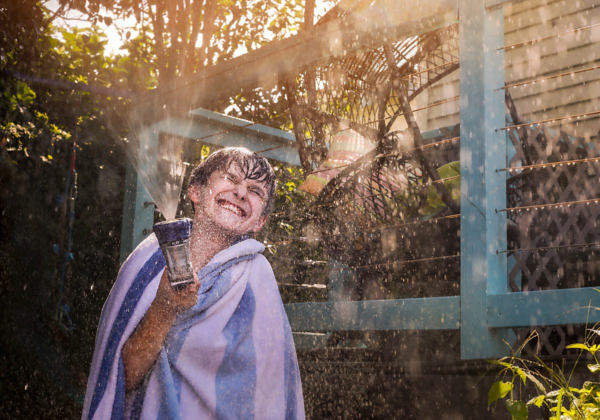 A little boy smiling while holding a sprinkler.