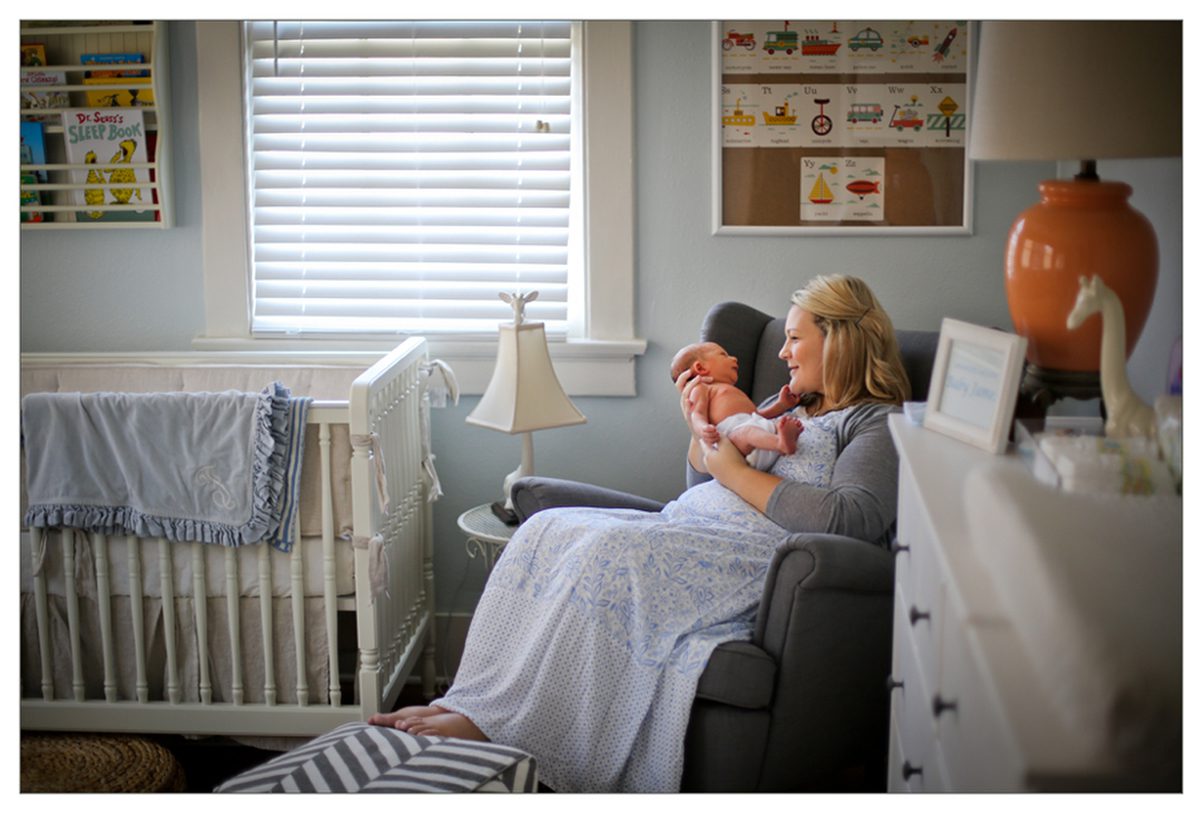 A mom cradling her newborn son in a nursery during their New Orleans lifestyle newborn session by Twirl Photography.