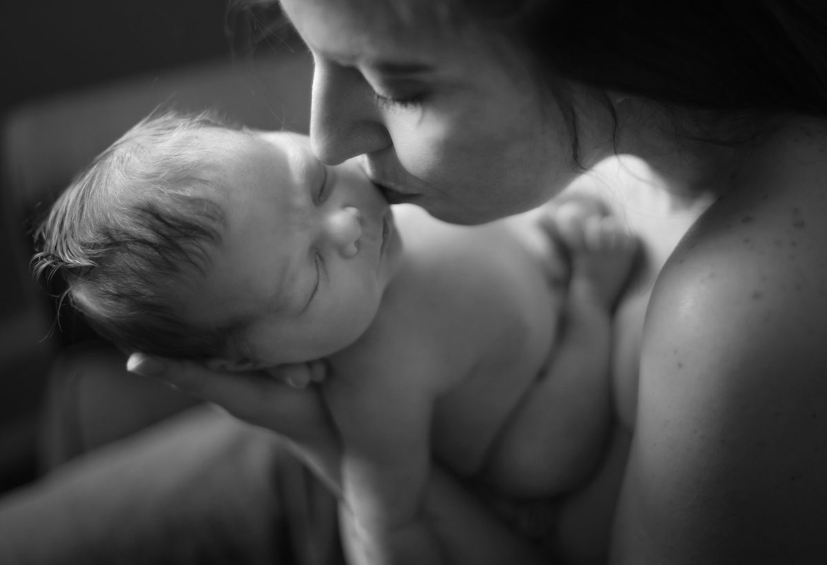 A mom kissing the cheek of her newborn child.