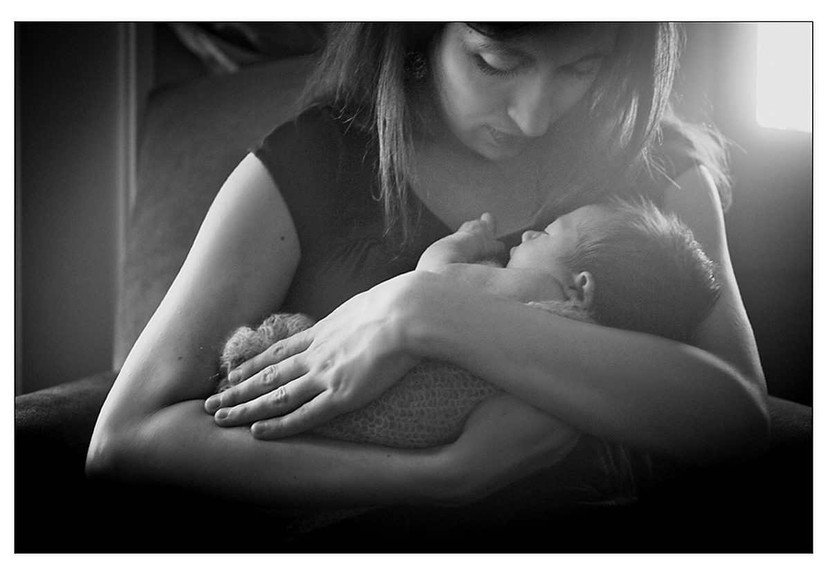 A mom cradling her newborn daughter in the baby's nursery during in home New Orleans lifestyle newborn session with Twirl Photography.