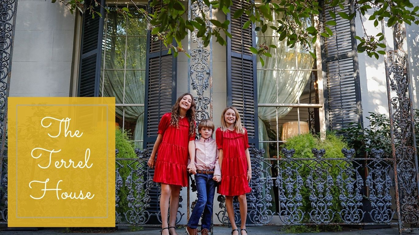 Three siblings standing on a porch with blue and grey iron work.