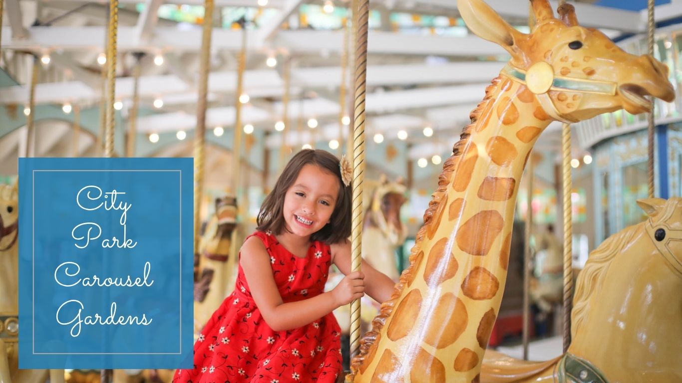 A girl wearing a red dress on a giraffe on a carousel smiling.