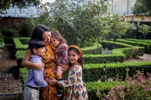 A mom hugging her three kids while wearing outfits in fall colors in a park.