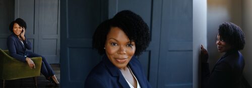 A woman looking at the camera wearing a blue blazer in front of a dark blue wall for headshot photogaphy.