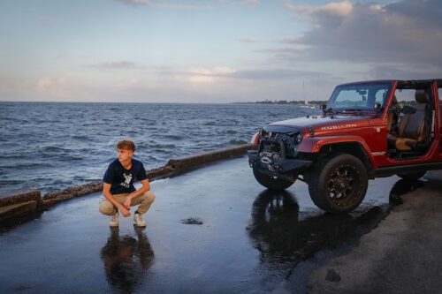 a man squatting next to a red jeep