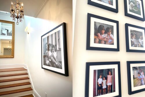 A large framed black and white family photo in a stairway with a big chandelier.