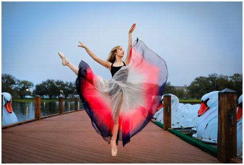 A young ballerina on point with a flowing skirt and arms in the air.