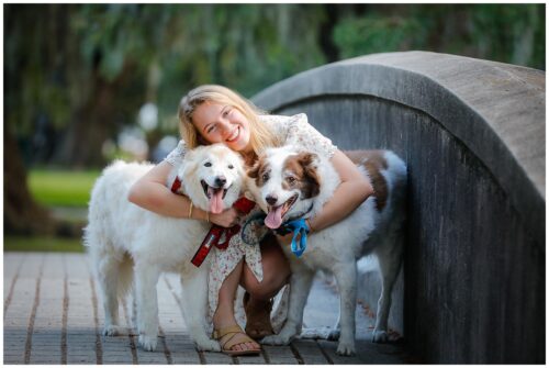 A high school graduate in a white dress hugging her two dogs for senior photos in New Orleans.