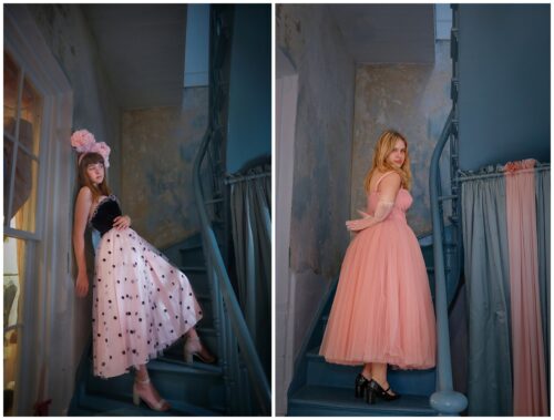 Two seniors in pink dresses standing in a stairwell.