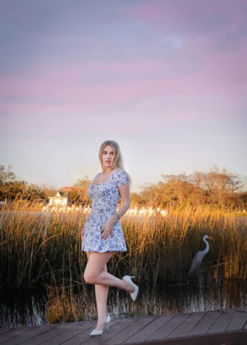 A senior graduate in a blue flower dress standing on a boardwalk in City Park during sunset.