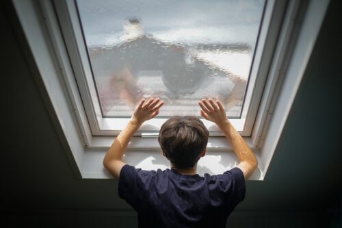 A boy looking out a window as it rains.