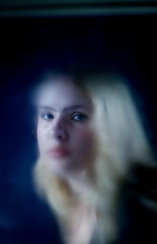 A girl looking through a window at the photographer.