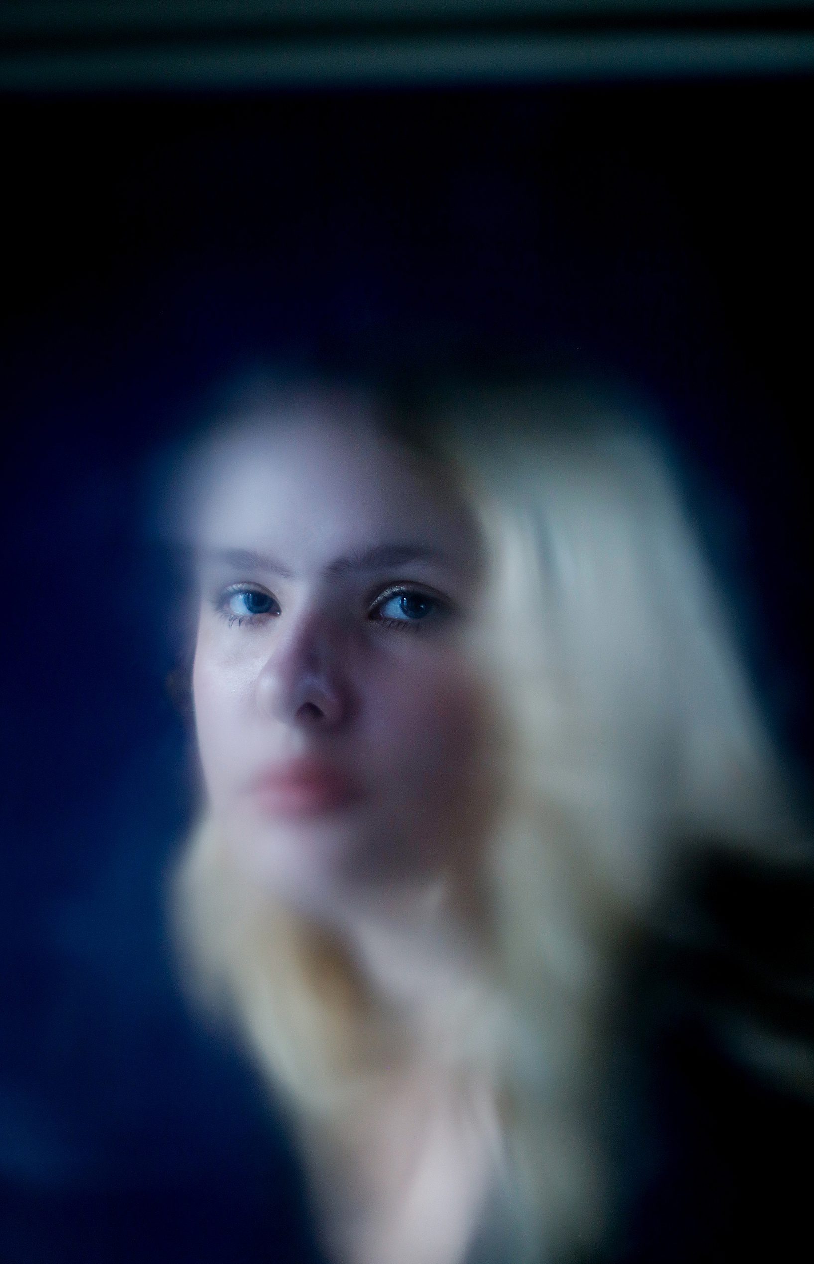 A girl looking through a window at the photographer.