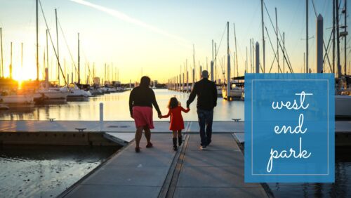 A mom and dad walking on a dock at sunset.