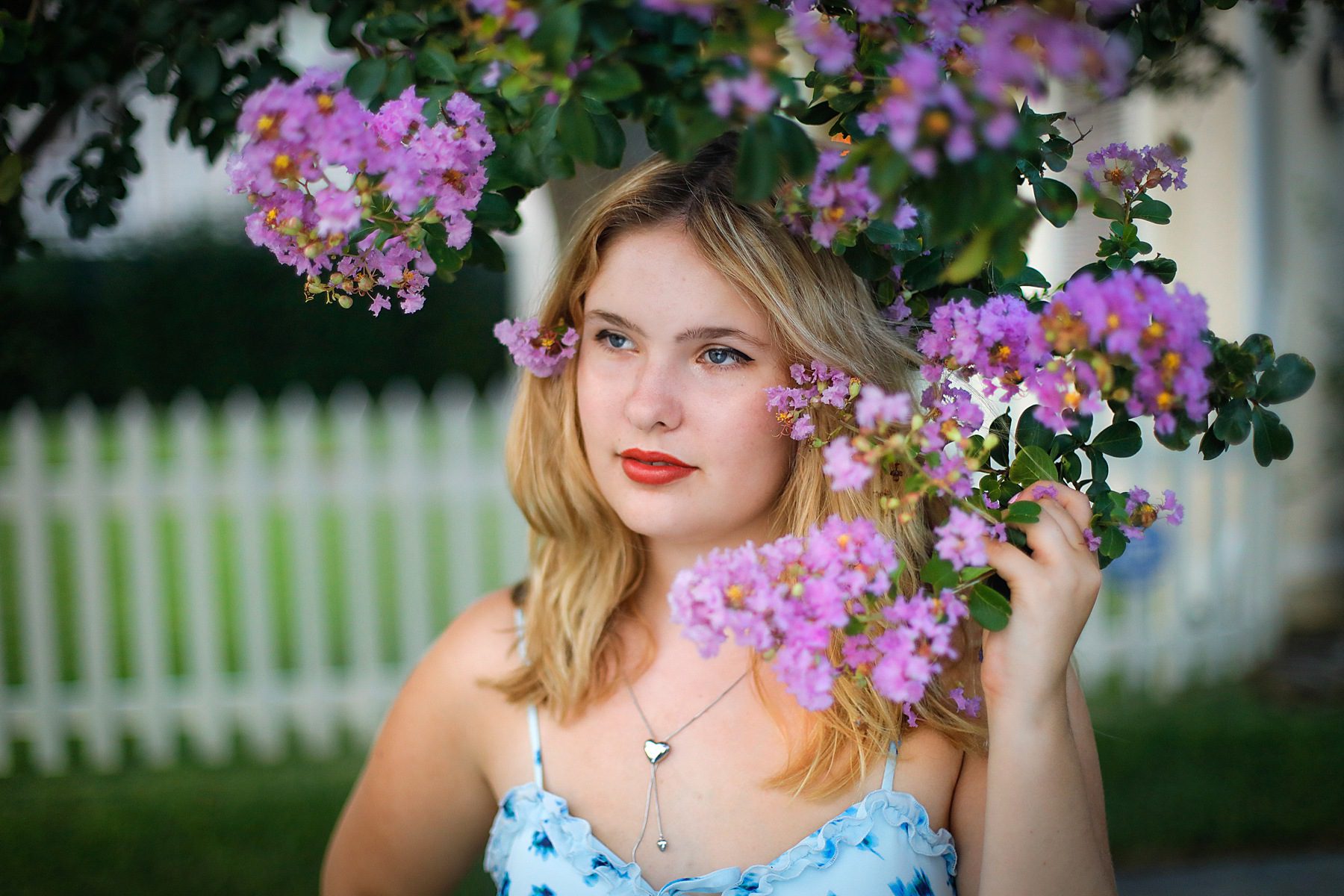A young woman standing surrounded by pink blooms.