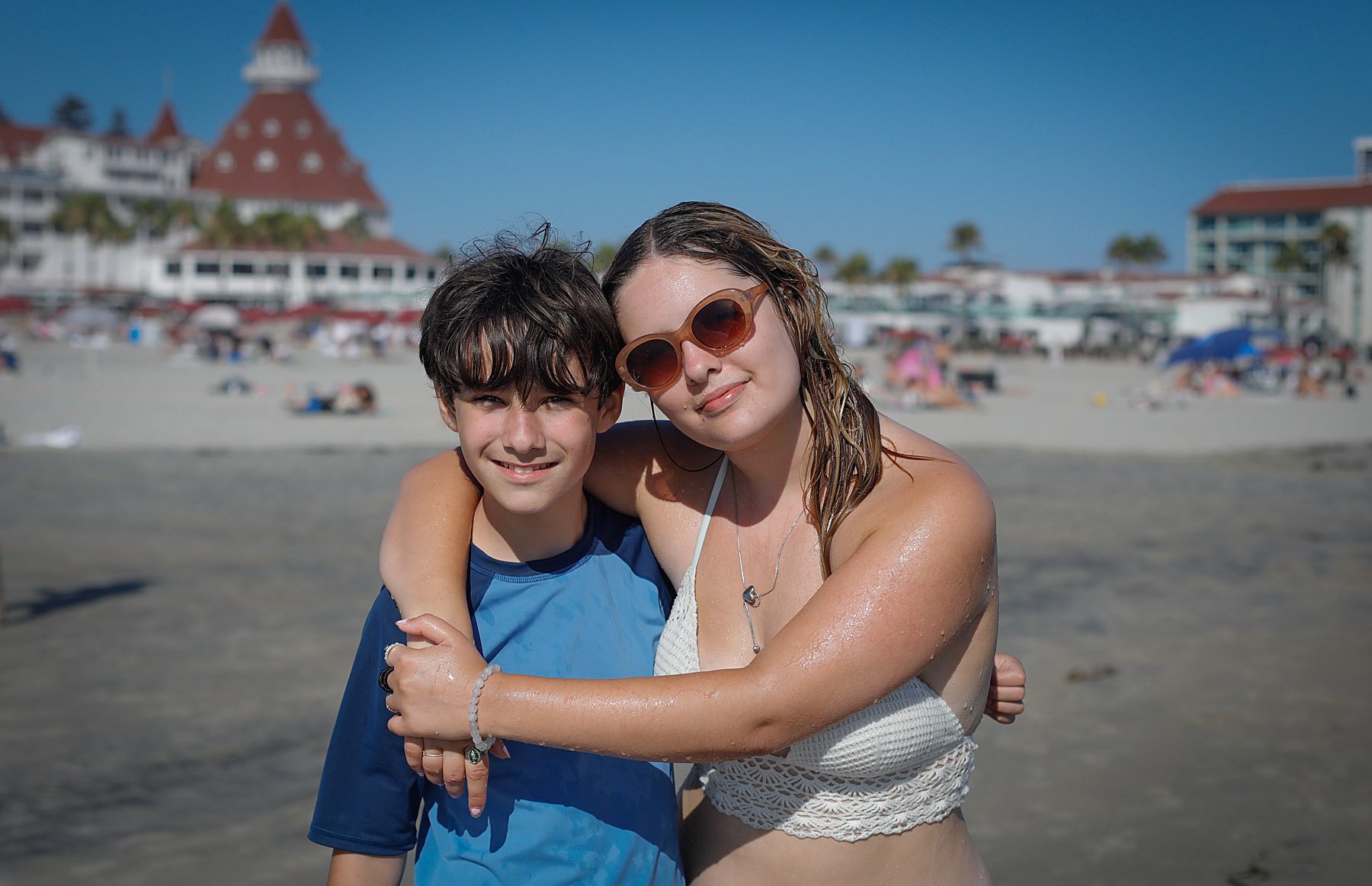 Two kids smiling at the camera on the beach.