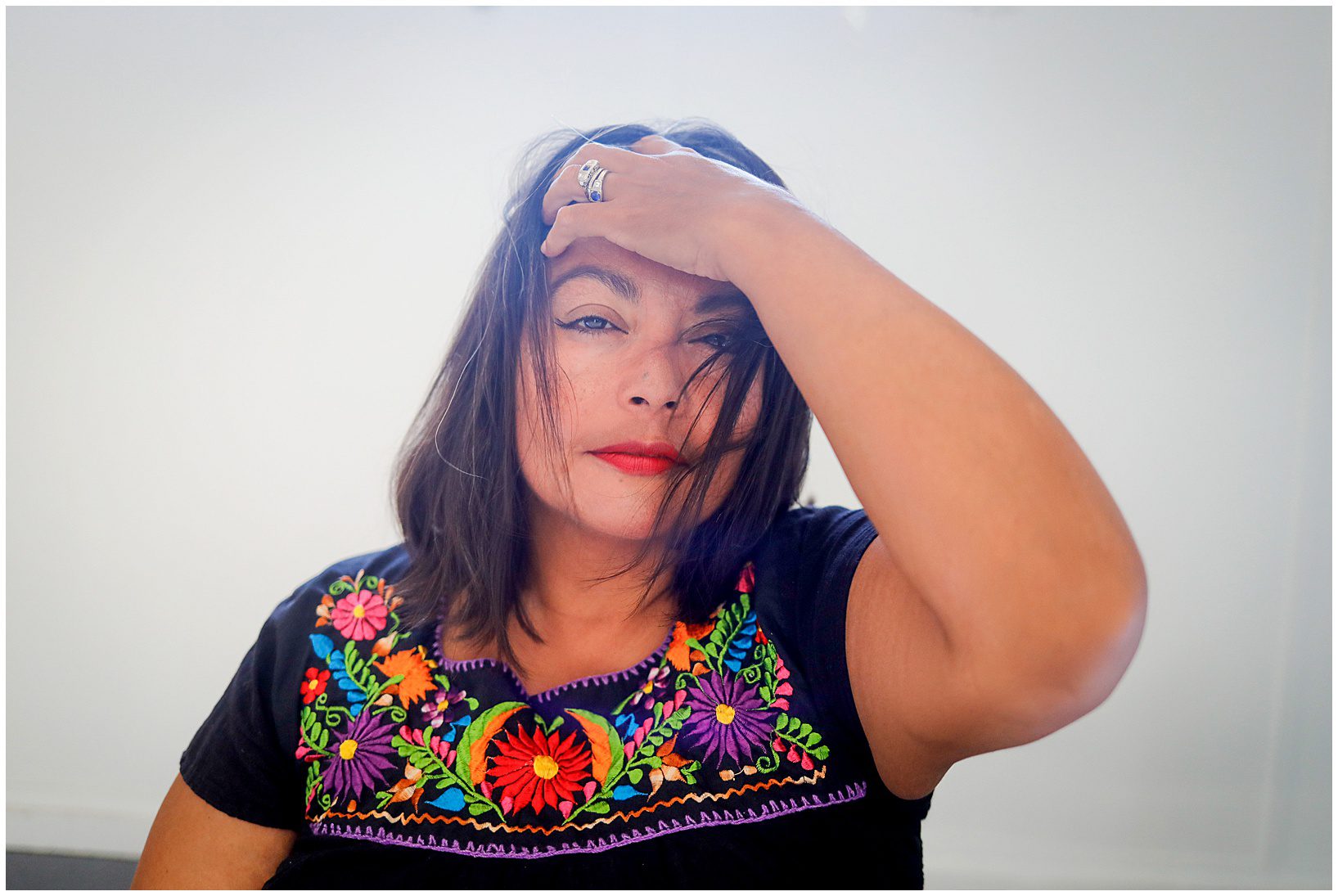 A woman wearing a black shirt pulling her hair back while looking at the camera.