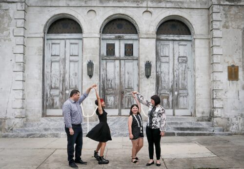 A family dancing in front of a big old building for a story about Behind-the-Scenes of a New Orleans Family Portrait Session: What Really Happens During Your Photo Adventure