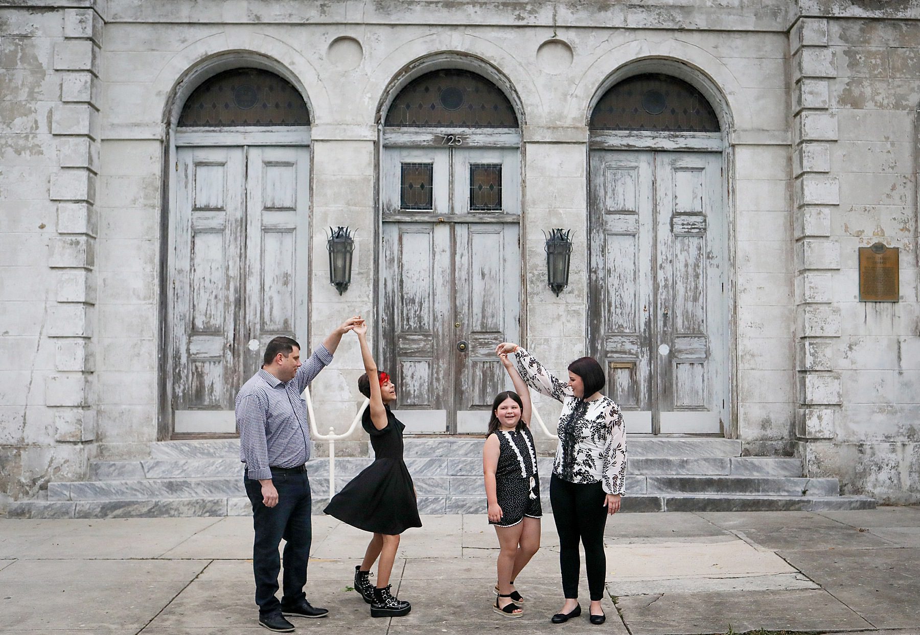A family dancing in front of a big old building for a story about Behind-the-Scenes of a New Orleans Family Portrait Session: What Really Happens During Your Photo Adventure