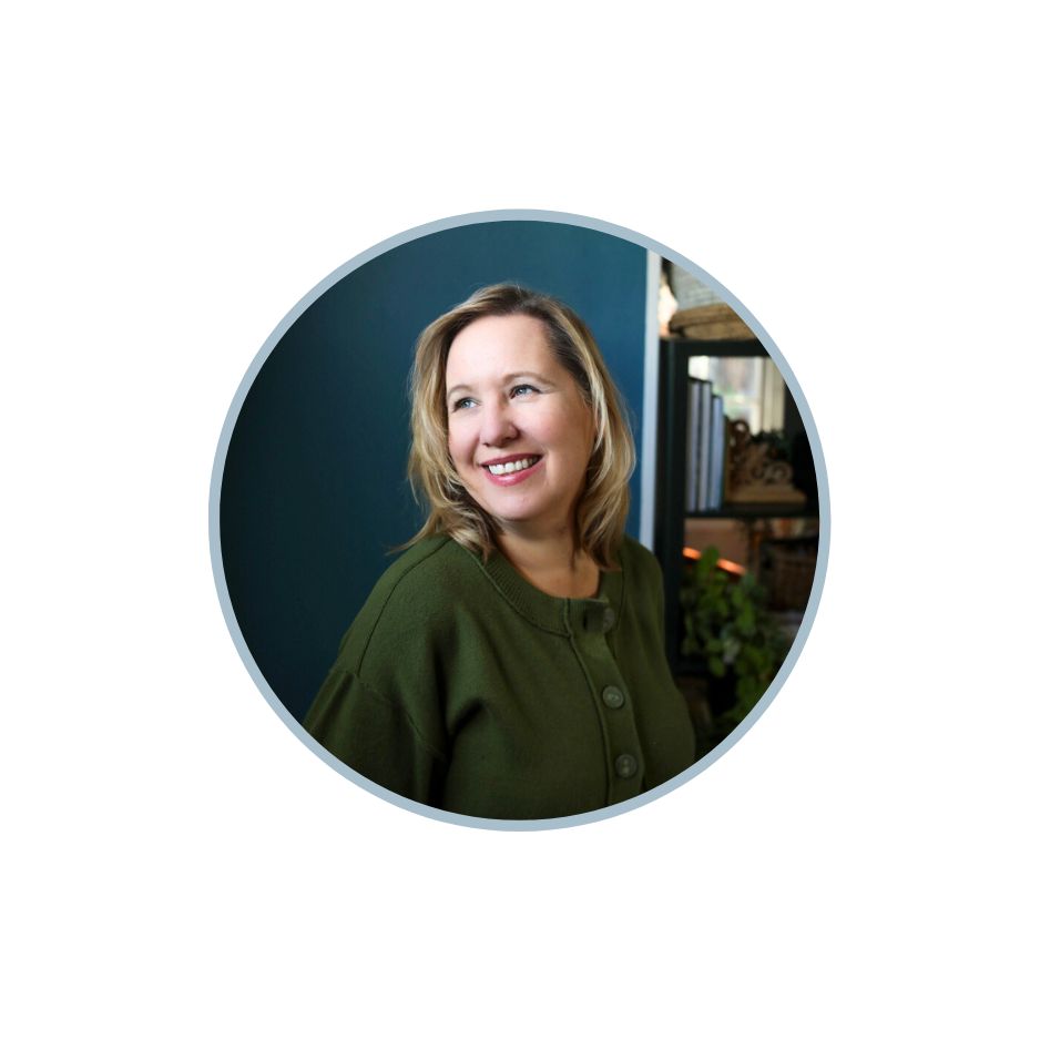 A photographer wearing a green sweater smiling near a window.