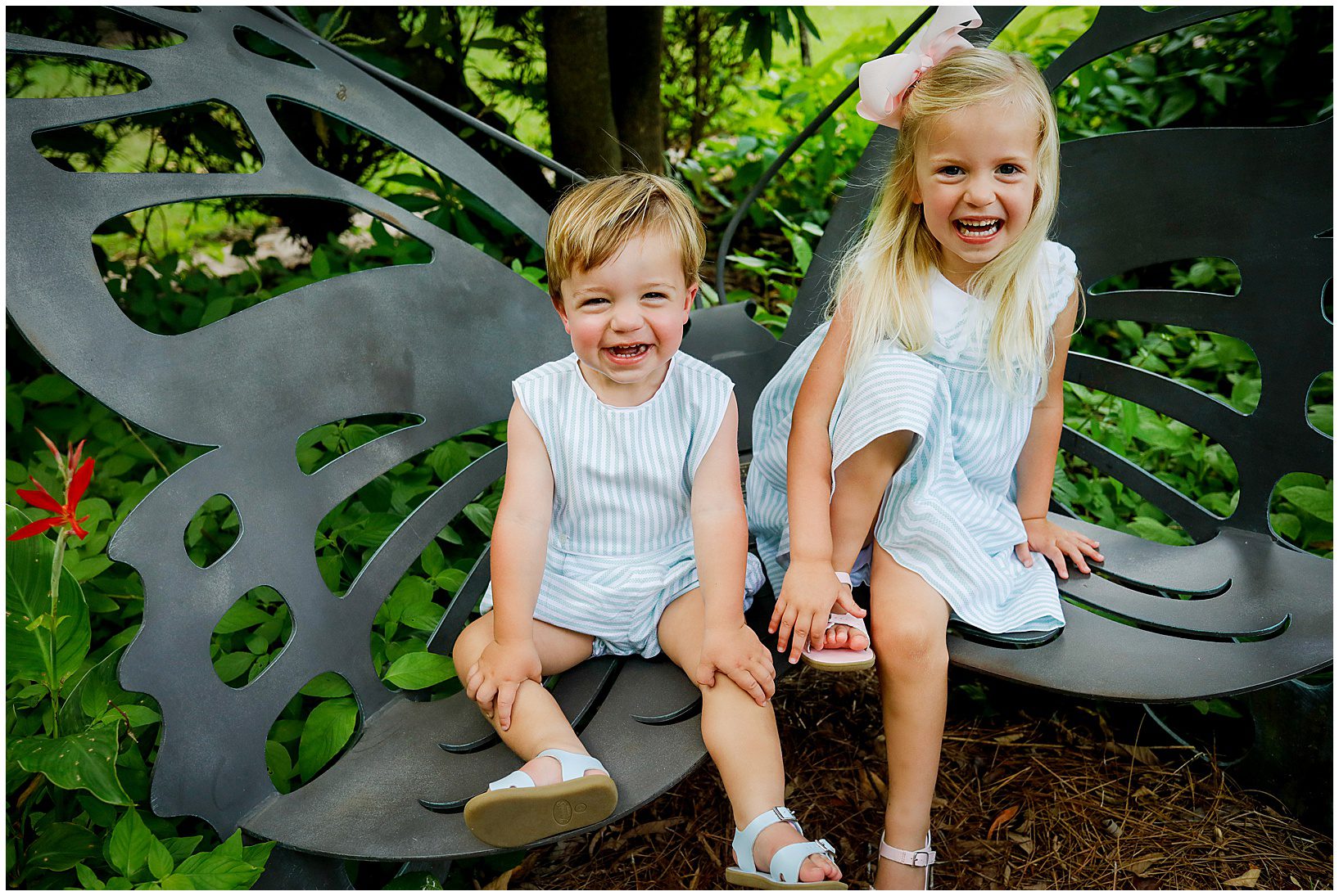 A little boy and his bigger sister wearing blue spring outfits sitting on a chair shaped like a butterfly.