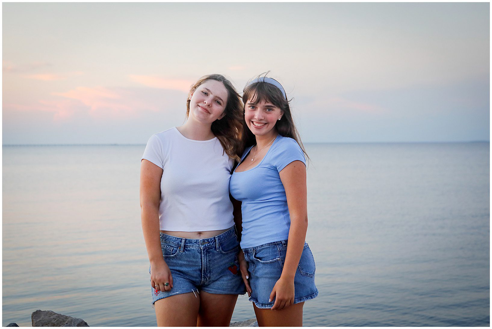 Two high school seniors standing next to each other for senior portraits near the lakefront.
