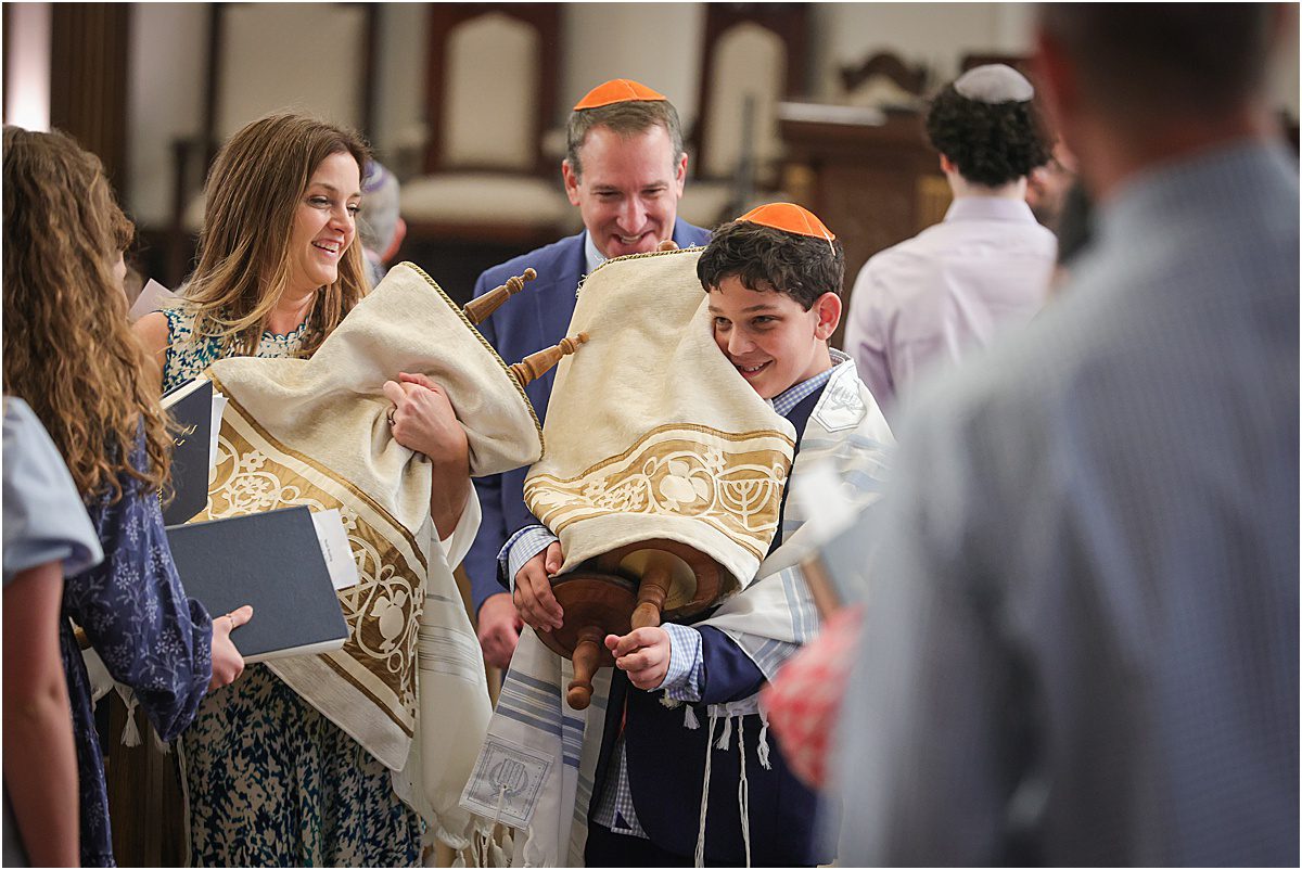 A boy holding the torah with a big smile during his bar mitzvah for a story about New Orleans Bar & Bat Mitzvah Photography: 5 moments you never want to miss.