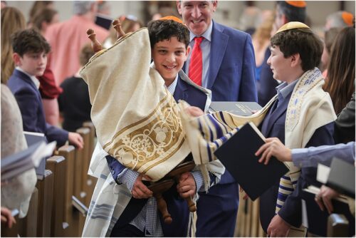 A boy holding the torah with a big smile during his bar mitzvah for a story about New Orleans Bar & Bat Mitzvah Photography: 5 moments you never want to miss.